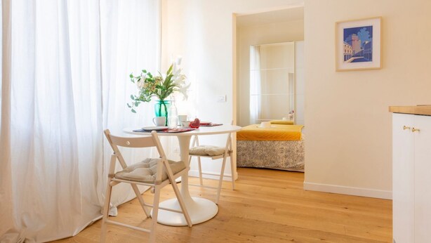 Un coin repas comprenant une table, des chaises, un vase avec des fleurs et un tableau accroché au mur.