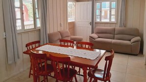 A living room with a beige sofa, a wooden dining table with chairs, and a large window with curtains. - Beautiful and Cozy House Surrounded by Nature (Morretes)