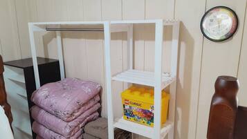 Um quarto com uma cama, um guarda-roupa, uma prateleira com cobertores dobrados, uma caixa de LEGO e um relógio de parede.
