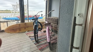 Una terrassa de fusta amb una taula de surf, una bicicleta i una banca.