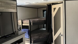 Ein kompaktes Wohnmobil-Interieur mit Etagenbett, Fernseher und Küchenzeile.