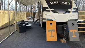 Ein Wohnmobil mit Überdachung, auf dessen Vorderseite 'MALLARD' steht, eine Holzlattenveranda und Gartenmöbel.