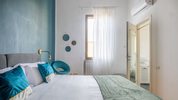 A modern bedroom with a bed, a chair, a radiator, and a bathroom visible through an open door. - Elegant Apartment with Two Bedrooms (Roma)