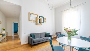 A modern living room with a grey sofa, teal chairs, a round dining table, and a vase of flowers. - Elegant Apartment with Two Bedrooms (Roma)