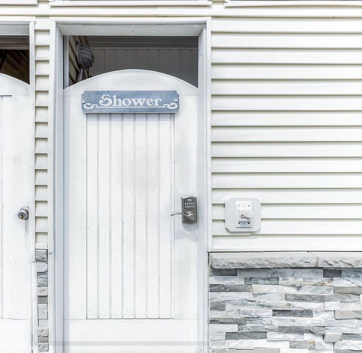 A white door with a 'Shower' sign above it, a keypad lock, and a stone accent wall.