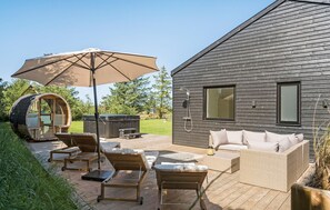 A wooden deck with lounge chairs and a hot tub, a large umbrella, and a modern house with a hot tub and outdoor shower. - Gorgeous home in Saltum with sauna (Saltum)