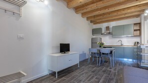 Una cocina moderna con estufa integrada, un comedor con mesa y sillas, y un televisor sobre un mueble blanco.