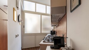Une cuisine compacte équipée d’une cuisinière à gaz, d’une machine à café et d’un petit coin repas avec un panier rempli d’assiettes.