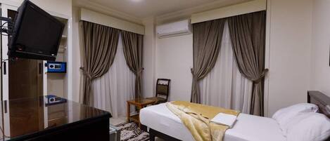 Una habitación de hotel con cama, escritorio, computadora, teléfono y cortinas.