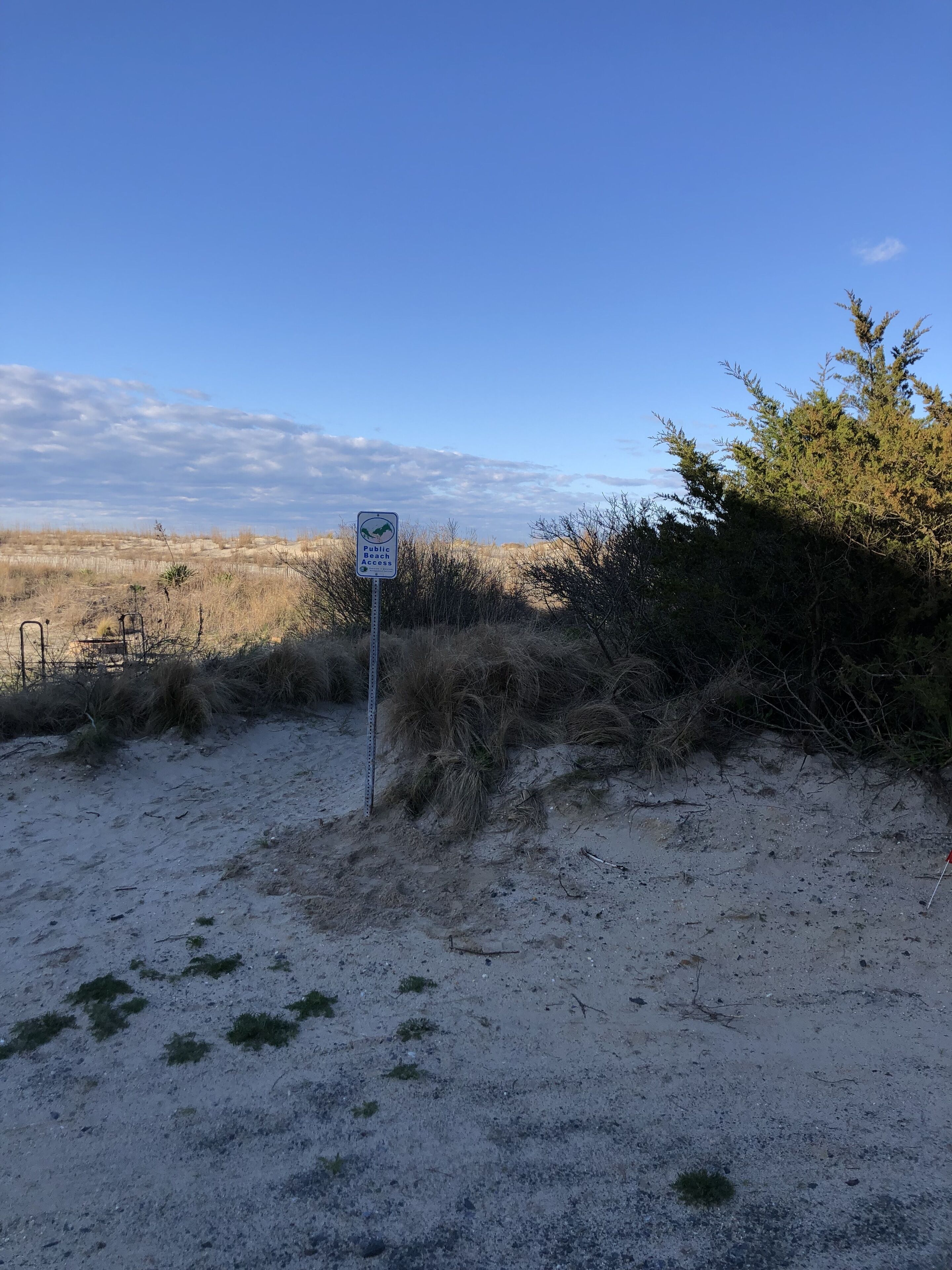 Ein sandiger Bereich mit einem Schild, das den Zugang zum öffentlichen Strand anzeigt.