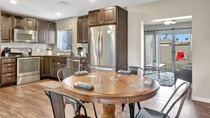 A modern kitchen with stainless steel appliances, a dining area with a wooden table, and a sliding glass door leading to a balcony. - Experience Scottsdale Charm: Cozy Retreat, Heated Pool, Family-Friendly Fun! (Scottsdale)