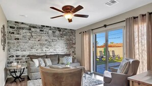 A living room with a brick wall, a ceiling fan, a sofa, a coffee table, and a view of the outside through large sliding doors. - Experience Scottsdale Charm: Cozy Retreat, Heated Pool, Family-Friendly Fun! (Scottsdale)