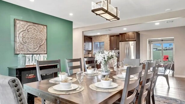 A dining area with a wooden table set for four, surrounded by chairs. There is a decorative wall piece above the table and a modern chandelier hanging above. - Experience Scottsdale Charm: Cozy Retreat, Heated Pool, Family-Friendly Fun! (Scottsdale)