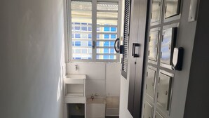 A narrow hallway with a window, a small sink, and a door with multiple locks. - 405 Moderno Aparta-Suite en Versalles Tipo Loft - Cali Tower Suites & Lofts (Cali)