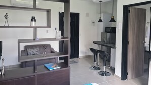 A modern hotel room with a dark wood desk, a comfortable sofa, a small dining area with two bar stools, and a large mirror. - 405 Moderno Aparta-Suite en Versalles Tipo Loft - Cali Tower Suites & Lofts (Cali)