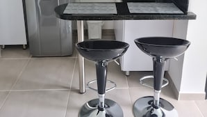 A modern kitchen with a black countertop, two bar stools, a refrigerator, a microwave, and pendant lights. - 405 Moderno Aparta-Suite en Versalles Tipo Loft - Cali Tower Suites & Lofts (Cali)