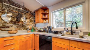 A kitchen with wooden cabinets, a stone wall, and a window with a view of trees. - Near Hiking: Pet-Friendly Sierra Valley Gem (Loyalton)