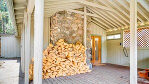 A covered wooden deck with a stone wall and a stack of firewood. - Near Hiking: Pet-Friendly Sierra Valley Gem (Loyalton)