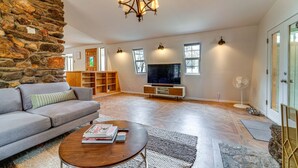 A spacious living room with a stone wall, a grey sofa, a wooden coffee table, a TV, and a stone fireplace. - Near Hiking: Pet-Friendly Sierra Valley Gem (Loyalton)