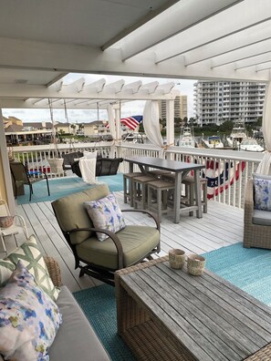Una terraza con asientos al aire libre, incluyendo sillas y una mesa, con vista a un puerto deportivo con barcos y un edificio al fondo.
