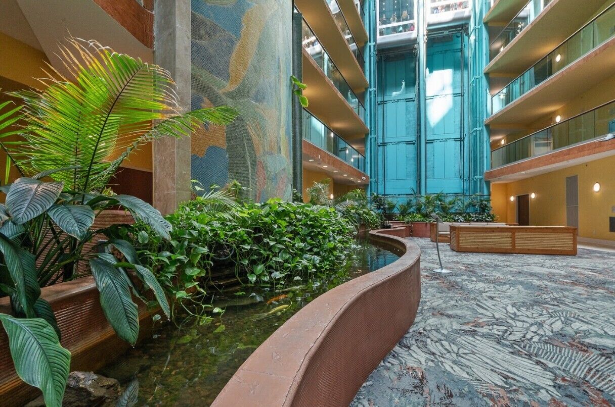 En hotelllobby med en central fontän, inomhusväxter och ett högt tak med balkonger.