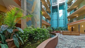 Un atrium d’hôtel doté d’un élément décoratif central avec de l’eau, de plantes d’intérieur et d’un haut plafond agrémenté de balcons.