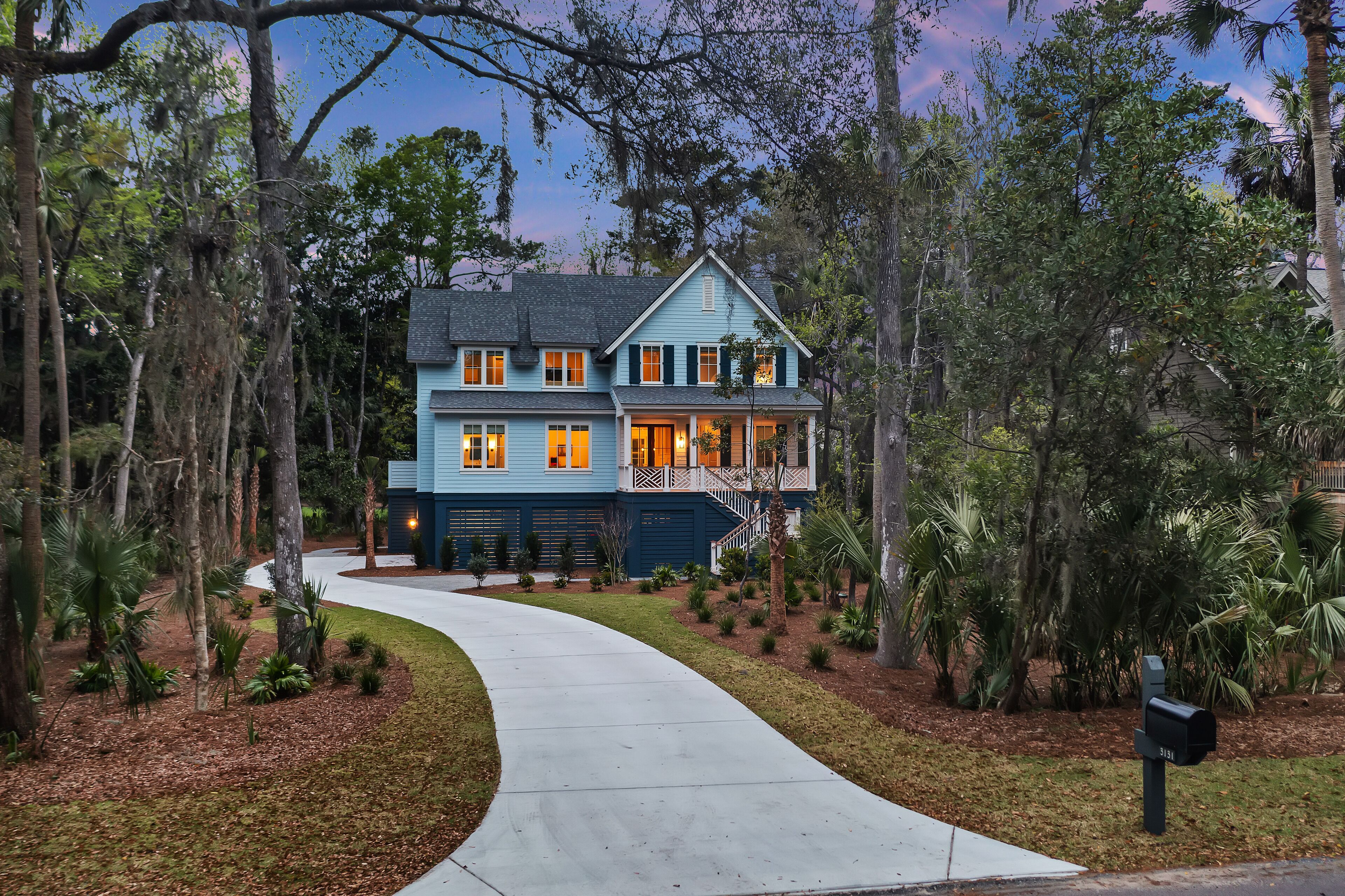 A two-story house with a curved driveway, surrounded by dense trees and a well-maintained lawn.