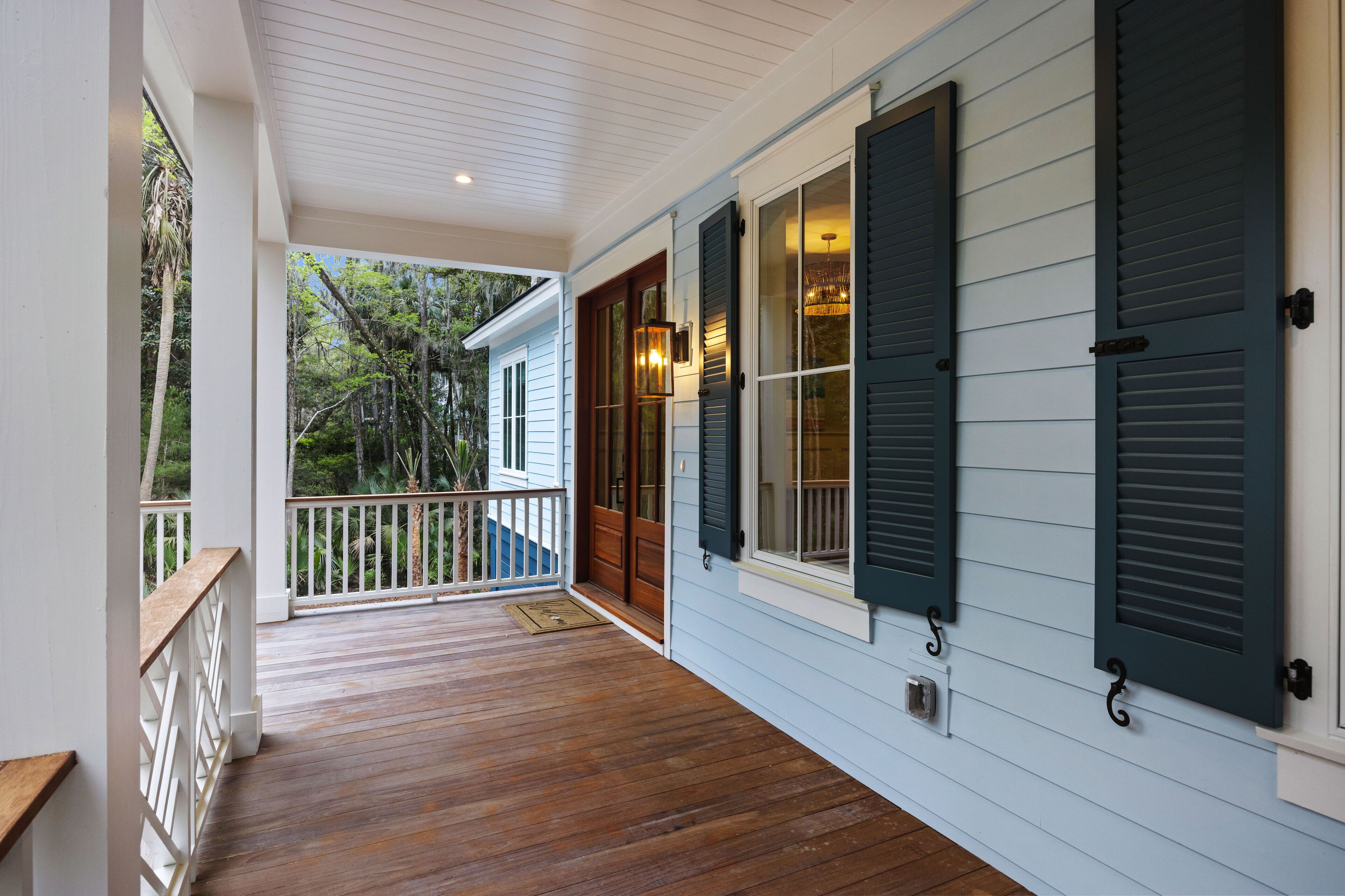 A covered porch with wooden flooring, white railings, and a view of a forested area.