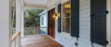 A covered porch with wooden flooring, white railings, and a view of a forested area.