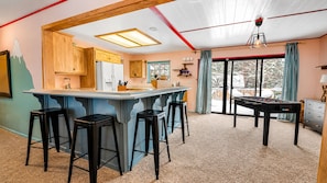 Een keuken met houten kasten, een bar met krukken, een tafelvoetbaltafel en een groot raam met uitzicht.