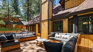 A wooden cabin with a deck, furnished with sofas and a table. - Evergreen - Luxury 3BR | En-Suite, Hot Tub, Game Room (Big Bear Lake)