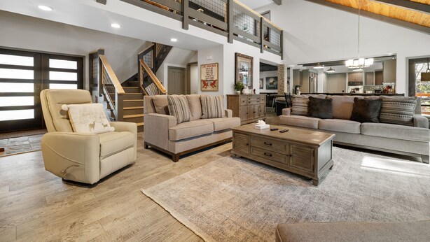 A spacious living room with a high ceiling, a staircase, and a kitchen in the background. - Evergreen - Luxury 3BR | En-Suite, Hot Tub, Game Room (Big Bear Lake)