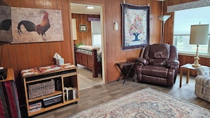 Una sala de estar acogedora con paneles de madera, un sillón de cuero marrón, una estantería, una alfombra grande y un colcha colgada en la pared.
