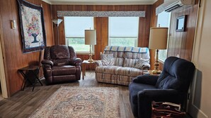 Una sala de estar acogedora con paredes de paneles de madera, una alfombra grande, un sillón de cuero, un sofá estampado y otro sillón azul.