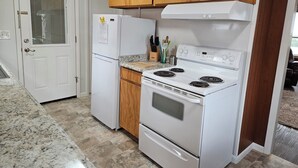 Una cocina con un refrigerador blanco, estufa y horno, armarios de madera y encimera de granito.