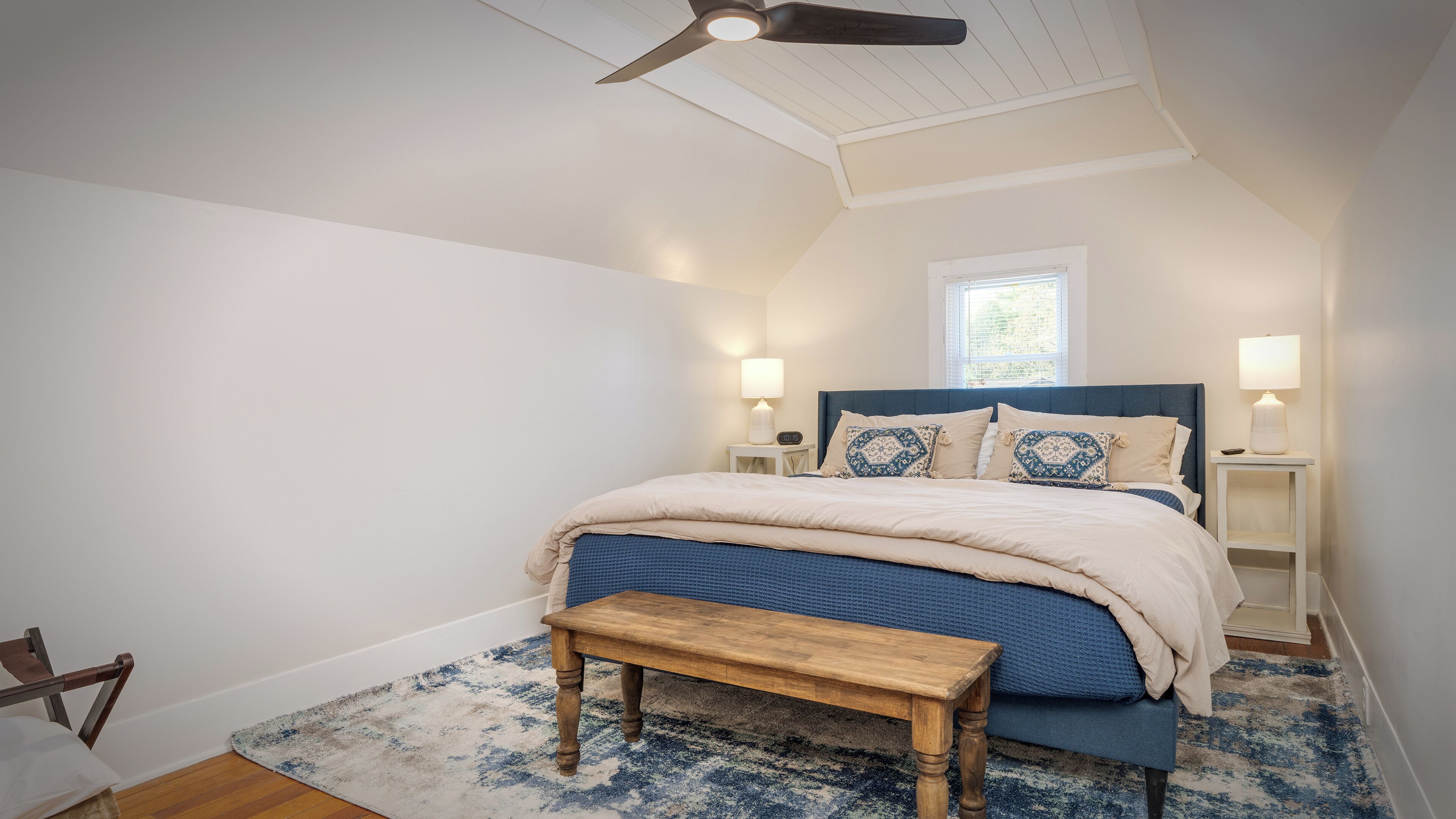 A bedroom with a bed, bedside lamps, a wooden bench, and a ceiling fan.
