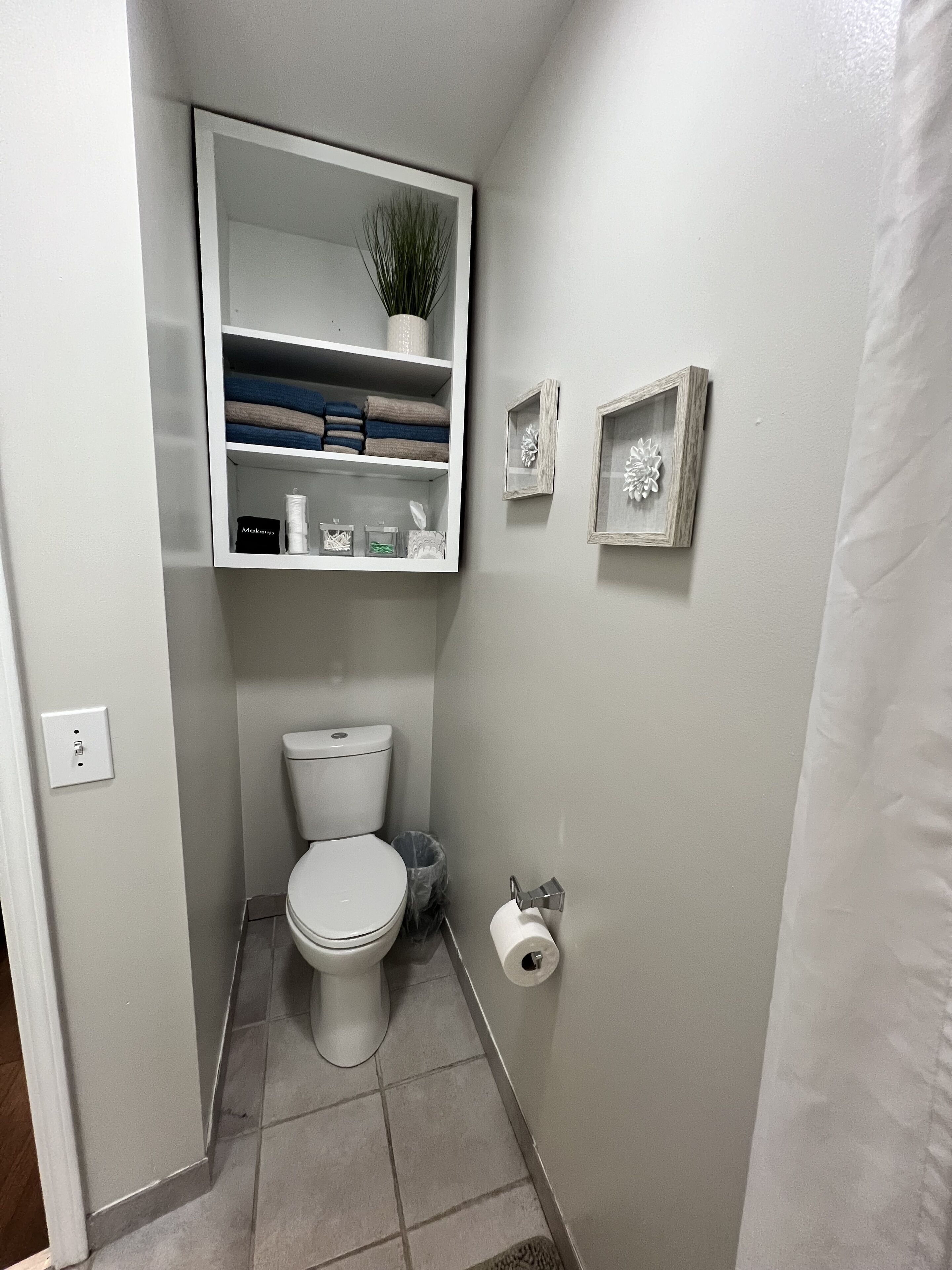 Een kleine, schone badkamer met toilet, een plankje met toiletartikelen en twee decoratieve lijsten aan de muur.