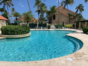 A clear swimming pool with lounge chairs and palm trees.
