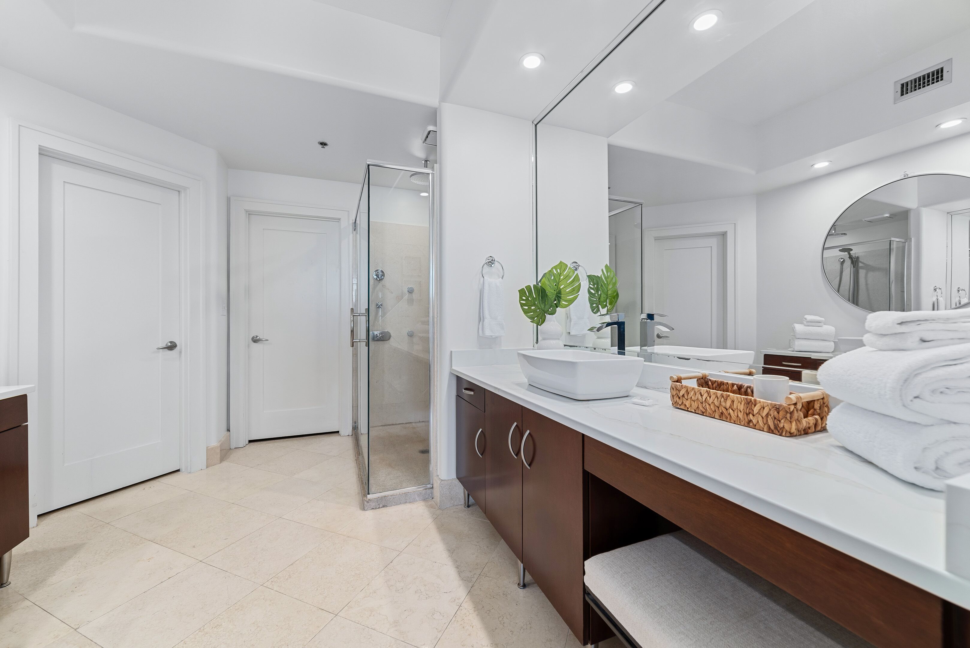 A modern bathroom with a large mirror, white vanity, and a glass shower enclosure.