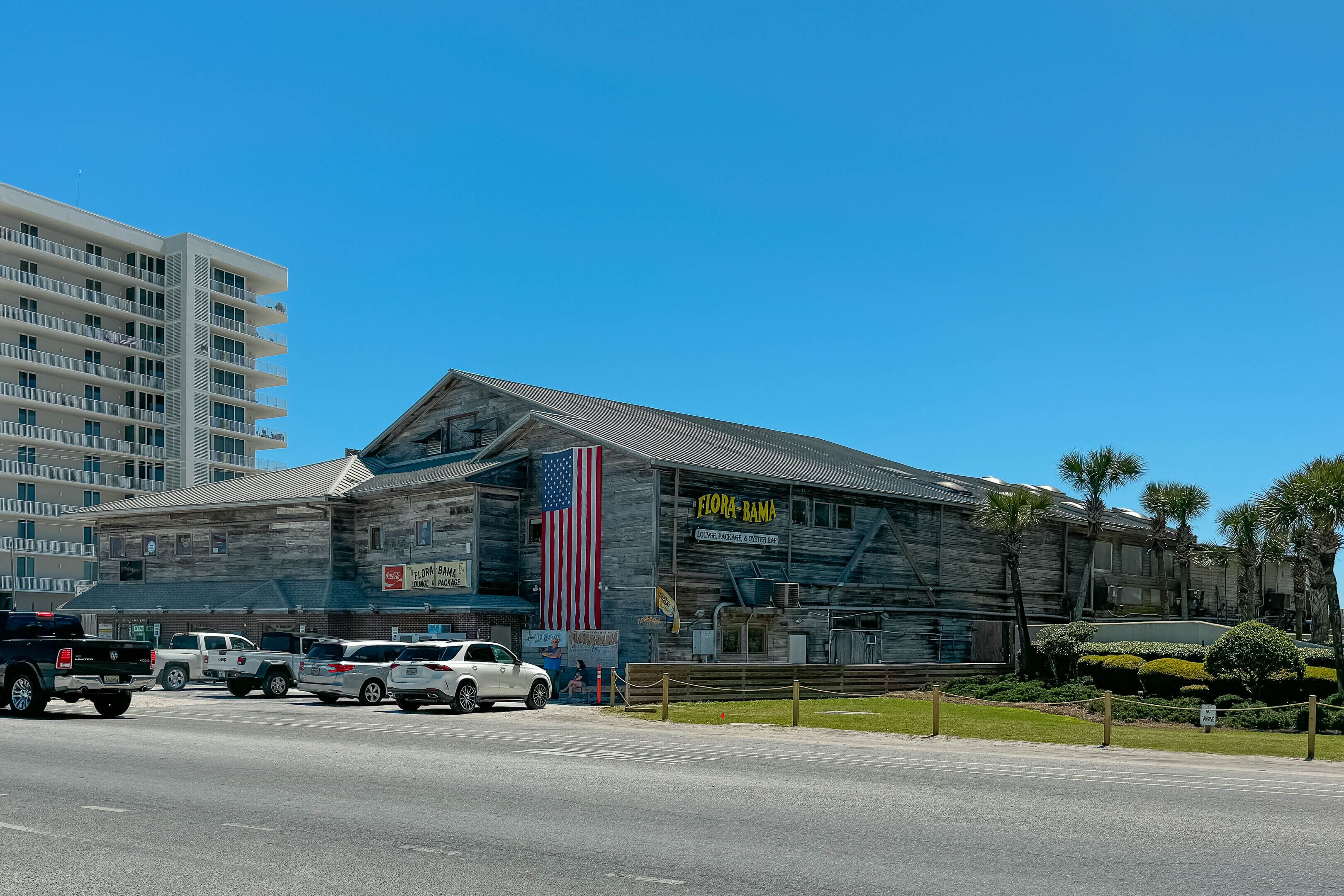 Un bâtiment orné d’un grand drapeau américain, une enseigne indiquant « Florm Bama » et un parking où sont stationnés plusieurs véhicules.