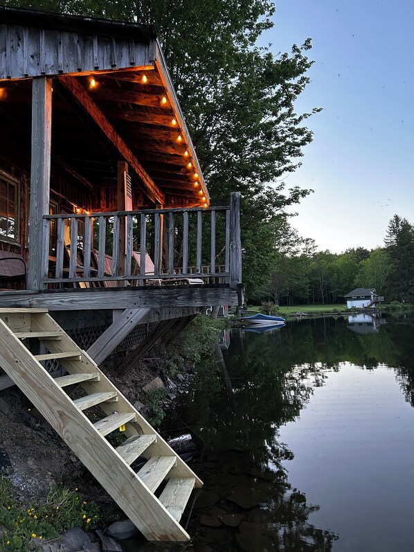 Une cabane en bois dotée d’une terrasse qui surplombe un lac paisible, le tout entouré d’arbres.