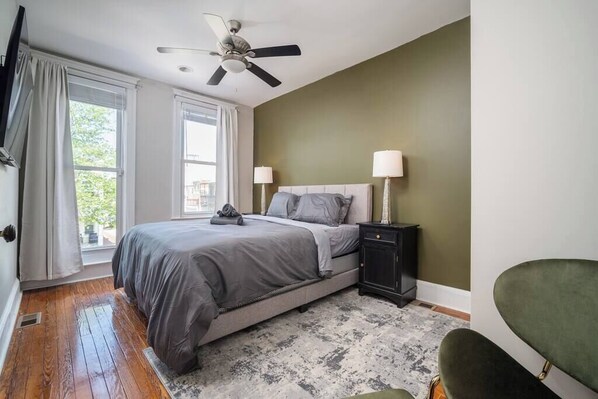 A bedroom with a bed, bedside tables, a ceiling fan, and a view through a window.
