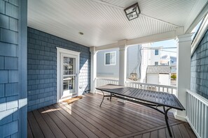 A covered porch with a wooden table and chairs, a white door, and a view of neighboring houses. - Rooftop Deck, Ocean Views & Elevator: Huge Home 6BR/4.5BA.  Steps from beach! (Ocean City)