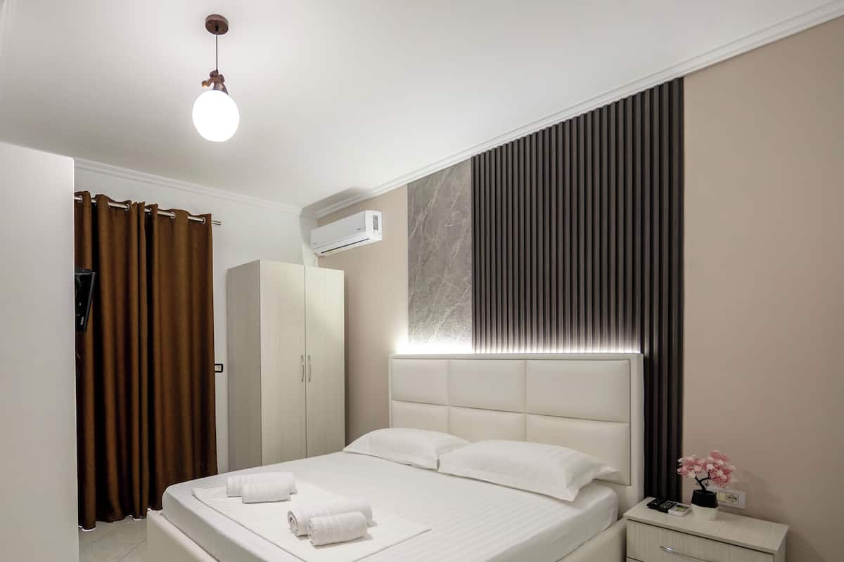 A modern bedroom with a large bed, a wardrobe, a bedside table, and a wall-mounted air conditioner.