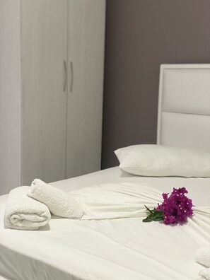 A neatly made bed with white linens, a white headboard, and a bouquet of purple flowers. - Flower Garden Villa (Ksamil)