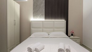A modern hotel room with a large bed, a wardrobe, a bedside table with a vase of flowers, and an air conditioning unit. - Flower Garden Villa (Ksamil)