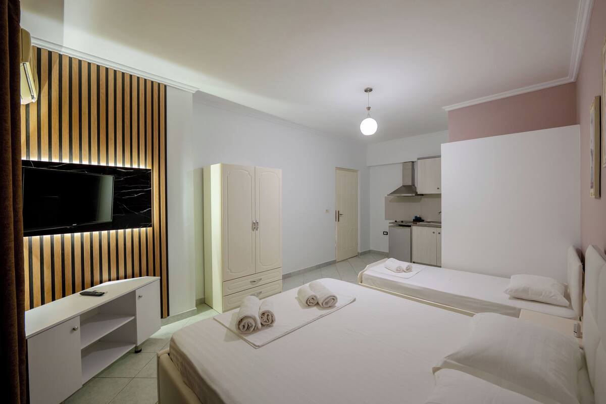 A hotel room with two beds, a TV, a desk, and a kitchenette.