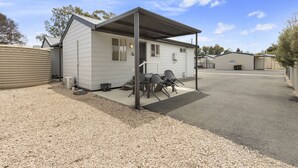 A single-story mobile home with a covered patio area, outdoor seating, and a gravel driveway.