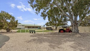 A building with a green roof, a gravel area, a bench, and a red tractor.