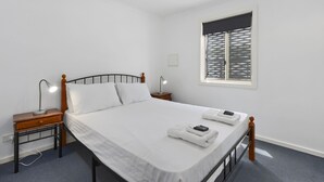 A neatly made bed with white linens, two bedside lamps, and a window with blinds.